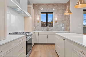 Kitchen featuring stainless steel gas stove, wall chimney exhaust hood, tasteful backsplash, pendant lighting, and light wood-type flooring