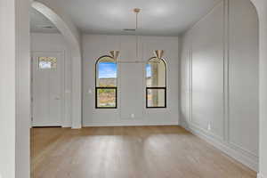 Unfurnished dining area featuring arched walkways, light wood-style floors, a decorative wall, and a chandelier