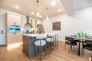 Kitchen featuring light brown cabinetry, tasteful backsplash, decorative light fixtures, an island with sink, and a breakfast bar