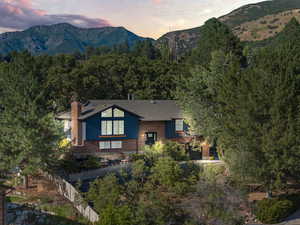View of front of house with a mountain view, brick siding, a chimney, and a forest view