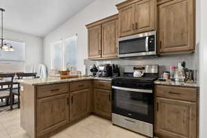 Kitchen with stainless steel appliances, a peninsula, tasteful backsplash, lofted ceiling, and decorative light fixtures