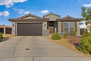 View of front of home with stone siding, a tile roof, concrete driveway, a garage, and stucco siding