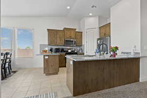 Kitchen with a peninsula, light stone countertops, light tile patterned floors, appliances with stainless steel finishes, and vaulted ceiling