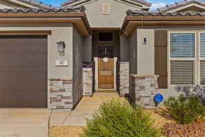 Entrance to property featuring a tile roof, stone siding, stucco siding, and an attached garage