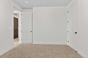 Unfurnished bedroom with light carpet and baseboards