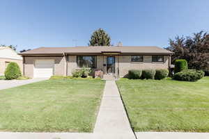 Ranch-style home featuring a garage, a front yard, concrete driveway, a chimney, and brick siding