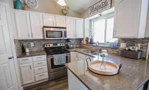 Kitchen with decorative backsplash, white cabinets, appliances with stainless steel finishes, dark stone counters, and dark wood-type flooring