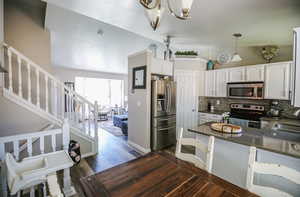 Kitchen featuring white cabinets, dark stone counters, appliances with stainless steel finishes, dark wood-type flooring, and decorative light fixtures
