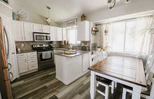 Kitchen with stainless steel appliances, white cabinets, backsplash, and vaulted ceiling