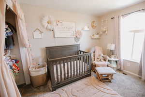 Carpeted bedroom with a crib and baseboards