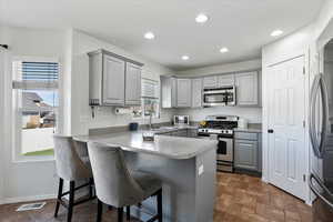 Kitchen featuring gray cabinets, stainless steel appliances, a peninsula, a kitchen breakfast bar, and light countertops