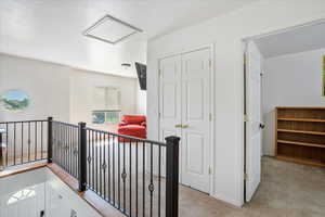 Hallway with light colored carpet, an upstairs landing, and a textured ceiling