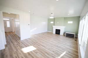 Unfurnished living room featuring plenty of natural light, a brick fireplace, light wood-style floors, and recessed lighting