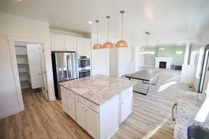 Kitchen with light wood finished floors, stainless steel appliances, a kitchen island, white cabinetry, and recessed lighting