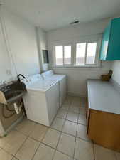 Laundry room with plenty of natural light, a textured ceiling, cabinet space, light tile patterned floors, and washing machine and dryer