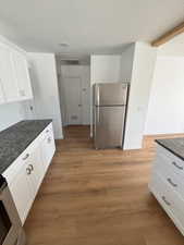 Kitchen with white cabinetry, appliances with stainless steel finishes, light wood-style flooring, dark stone counters, and a textured ceiling