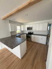 Kitchen featuring appliances with stainless steel finishes, dark wood-type flooring, a peninsula, white cabinetry, and a textured ceiling