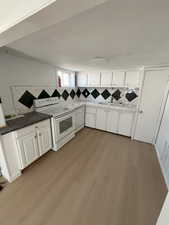 Kitchen featuring white cabinets, white appliances, backsplash, light wood finished floors, and dark stone counters