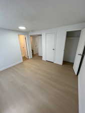 Unfurnished bedroom featuring light wood-type flooring, multiple closets, a textured ceiling, and connected bathroom