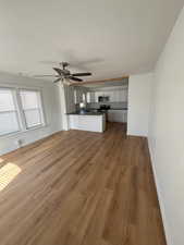 Unfurnished living room featuring dark wood-style flooring, a textured ceiling, and a ceiling fan
