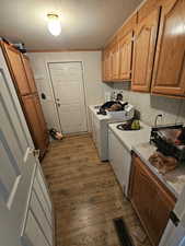 Laundry room featuring dark wood-type flooring, independent washer and dryer, a textured ceiling, ornamental molding, and cabinet space