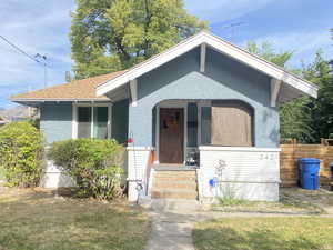 Bungalow featuring a shingled roof, a front lawn, a porch, and stucco siding