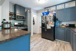 Kitchen with dark countertops, stainless steel appliances, light wood-type flooring, and blue cabinets