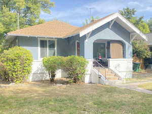 View of front of house with roof with shingles, a front yard, and covered porch