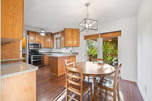 Kitchen featuring pendant lighting, brown cabinetry, stainless steel appliances, dark wood-style floors, and a peninsula