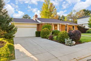 Ranch-style home with covered porch, brick siding, an attached garage, and driveway