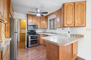 Kitchen featuring appliances with stainless steel finishes, dark wood-style flooring, a peninsula, and brown cabinetry