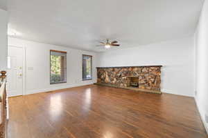 Unfurnished living room with wood finished floors, ceiling fan, a textured ceiling, and a stone fireplace