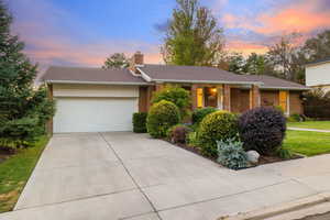 Ranch-style house featuring covered porch, a chimney, brick siding, an attached garage, and concrete driveway