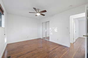 Unfurnished bedroom with dark wood-style floors, a closet, and a ceiling fan