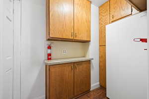 Kitchen with freestanding refrigerator, brown cabinets, and dark wood-style floors