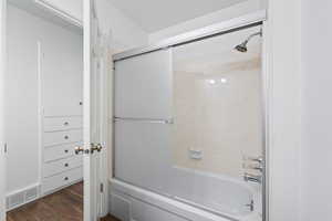 Full bathroom with enclosed tub / shower combo and dark wood-type flooring