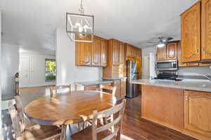 Kitchen with brown cabinets, a peninsula, dark wood-style floors, and appliances with stainless steel finishes