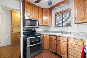 Kitchen with stainless steel appliances, dark wood-type flooring, brown cabinetry, and ceiling fan