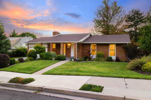 Single story home with a yard, brick siding, a porch, a chimney, and a shingled roof