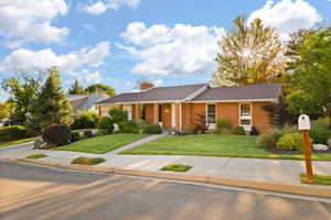 Single story home with a front yard, brick siding, a chimney, and covered porch
