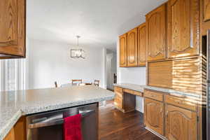 Kitchen with brown cabinetry, stainless steel dishwasher, dark wood finished floors, built in desk, and a textured ceiling