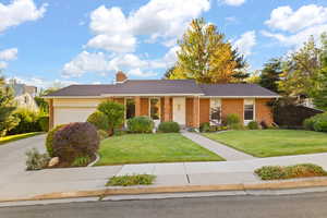 Ranch-style house featuring a porch, a front yard, a garage, a chimney, and brick siding