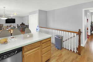 Kitchen featuring light countertops, light wood-type flooring, stainless steel dishwasher, pendant lighting, and open floor plan