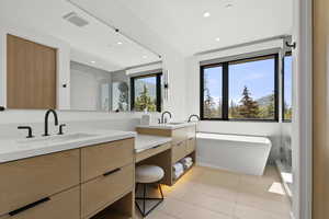 Full bath with a freestanding tub, vanity, light tile patterned flooring, recessed lighting, and two sinks