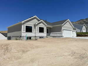 View of front of property with stone siding, board and batten siding, an attached garage, and driveway