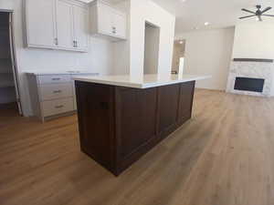 Kitchen featuring white cabinetry, dark brown cabinetry, a stone fireplace, light wood-style flooring, and recessed lighting