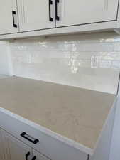 Detailed view of backsplash, white cabinetry, and light stone counters