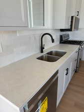 Kitchen featuring stainless steel appliances, decorative backsplash, white cabinets, and light stone countertops