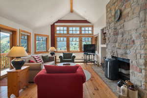 Living room featuring knotty pine floors a stone faced wood burning fireplace, along with walls of windows that lookout to fabulous views. French doors from this room lead out to a covered deck