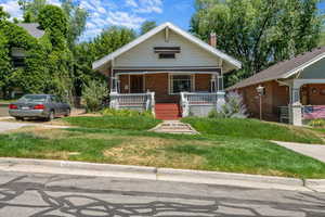 Bungalow-style house featuring covered porch, a chimney, a front yard, and brick siding